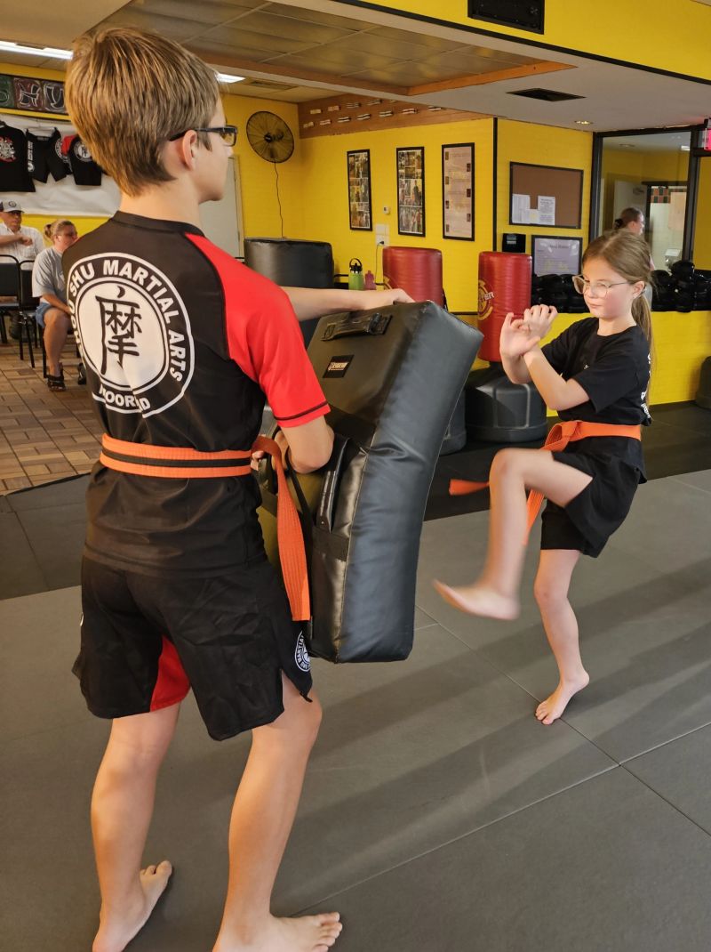 Teen student holding pads for a kicking drill