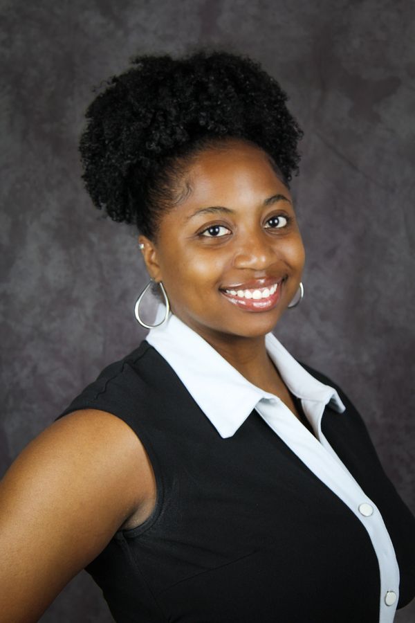 Confident woman with curly hair smiles warmly in professional attire.