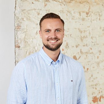 Ein Mann mit blauem Hemd vor einer weißen Ziegelwand.