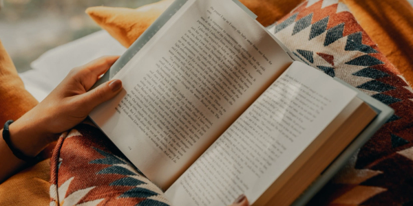 Person reading a book while relaxing on a patterned blanket.