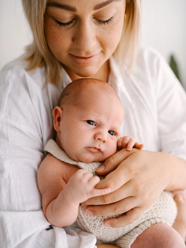 mother in a white shirt holding her newborn baby looking tenderly down at him