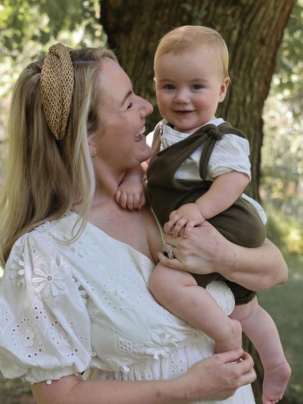 mother in white dress holding her baby smiling at him