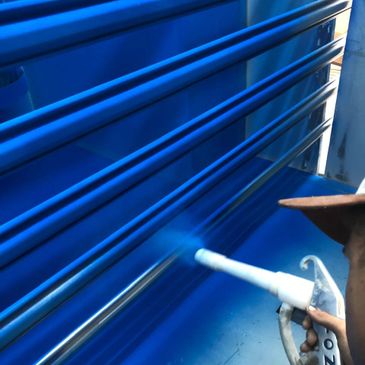 Person spray painting metal bars blue with a spray gun.