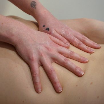 Hands massaging a back with lotion applied.