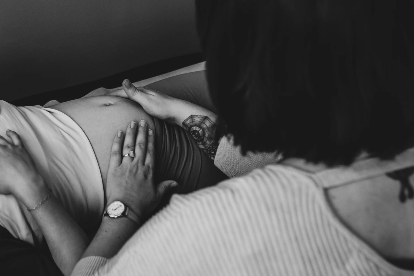 Pregnant woman lying down with another person touching her belly in a comforting manner.