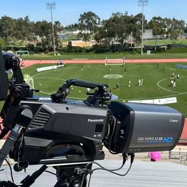 Professional video camera capturing a sports event at an outdoor stadium.