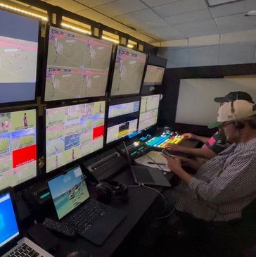 Technicians monitor multiple screens in a control room with laptops and communication headsets.