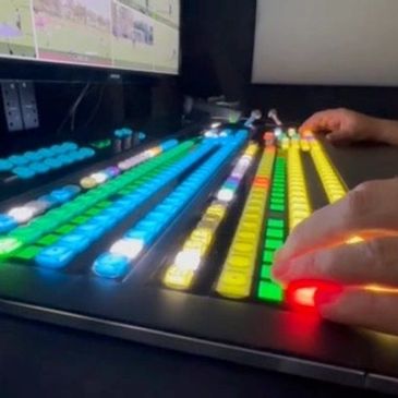 Hands operating a colorful video switcher with lit buttons.