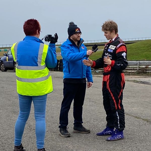 Racing driver being interviewed by a reporter with a camera operator filming.