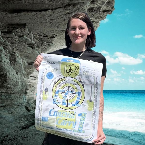 Young woman proudly holding a firearms instruction target by the ocean.