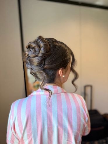 Elegant updo hairstyle with curled details on a woman in striped pink and white clothing.