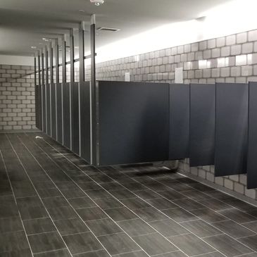 Row of black bathroom stalls in a tiled restroom.