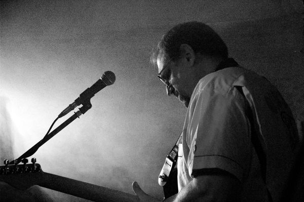 Man playing guitar on stage with microphone in black and white.