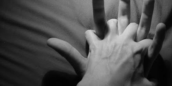 A black and white photo of two hands intertwined on a dark surface.