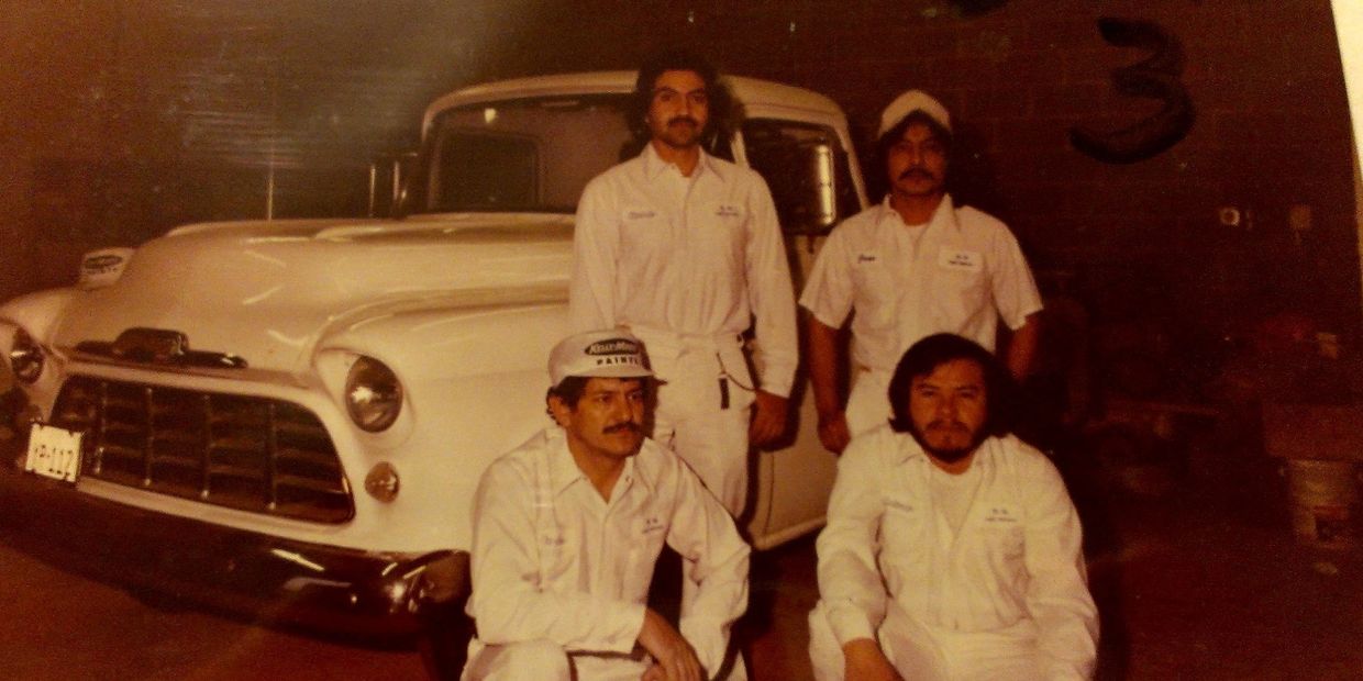Four men in white uniforms posing with a vintage white truck.