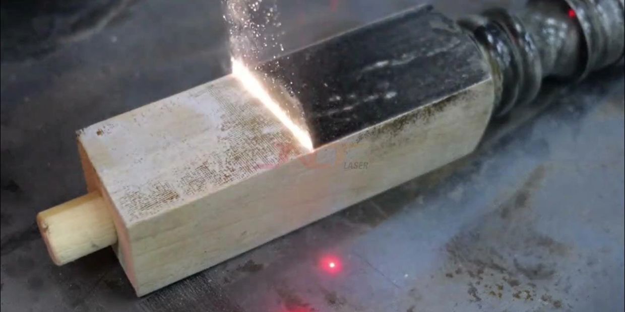 Laser cutting through a metal piece on a wooden block.