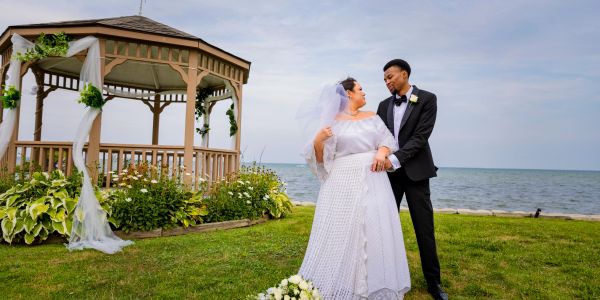 Bride and groom standing near a gazebo by the water.