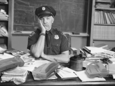 Tired policeman behind desk making useless phone calls while he tries to fundraise