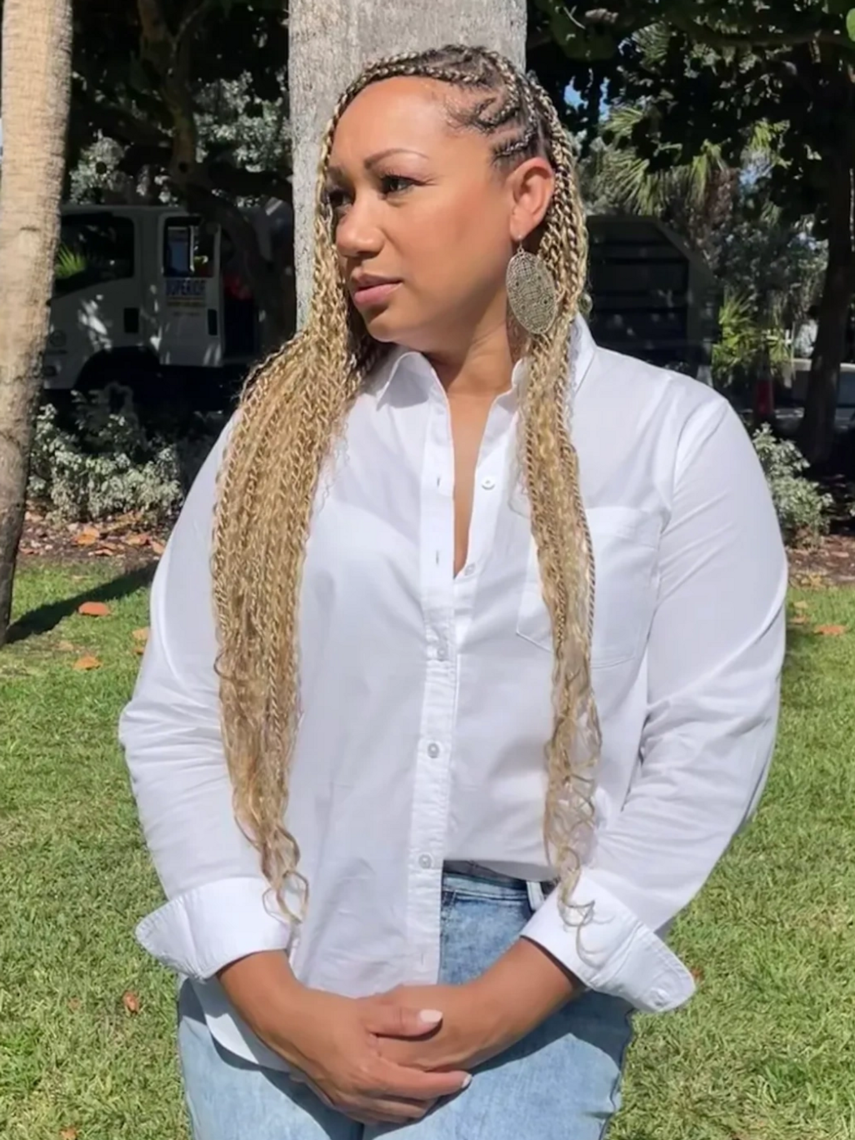 Woman with long braided hair in a white shirt and jeans standing outside.