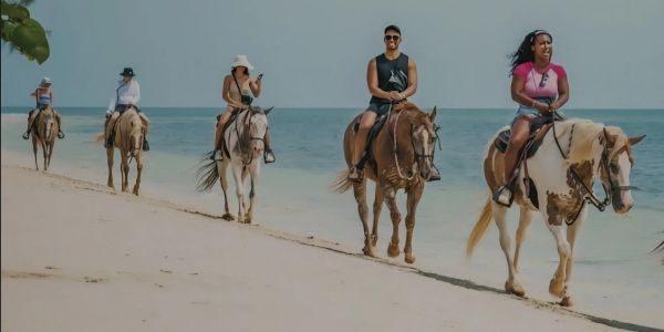 Group riding horses on a beach near the ocean.