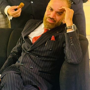 Man in pinstripe suit relaxing on a couch with a thoughtful expression.