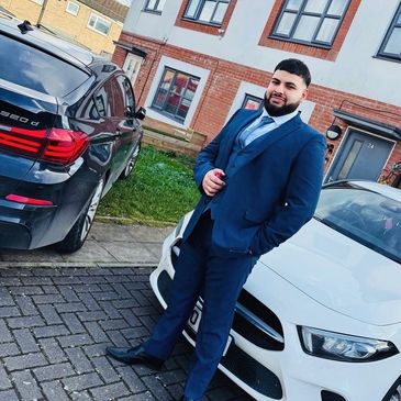 Man in a blue suit standing between two parked cars in a residential area.