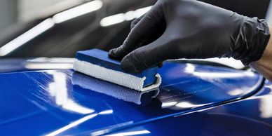 A gloved hand polishing a blue car surface with a sponge.