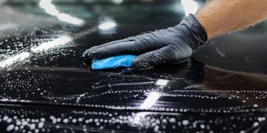 Hand with glove polishing a wet black car surface with a blue cloth.