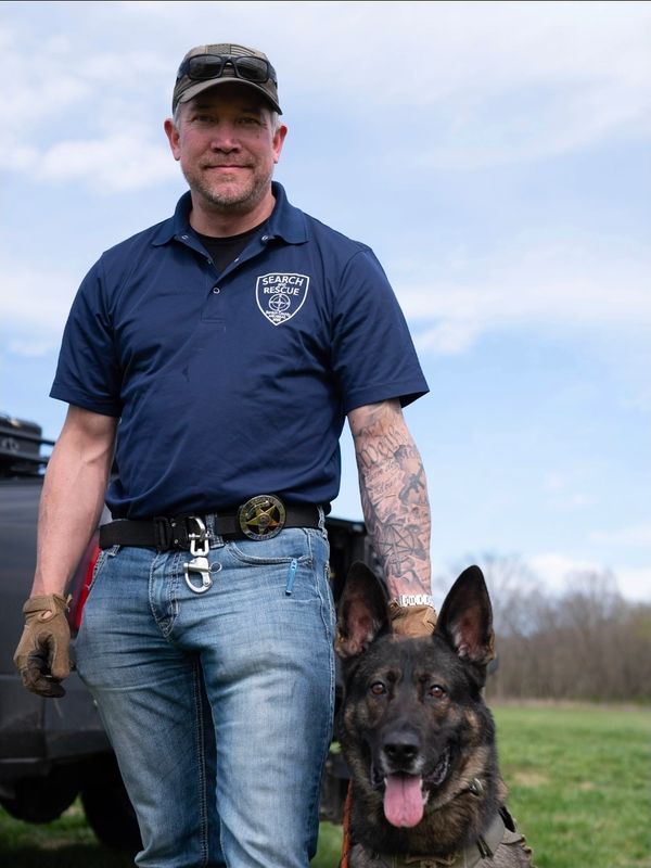 Search and rescue worker with a German Shepherd dog outdoors.