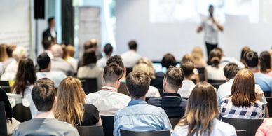 An audience listening to a male presenting on a large screen