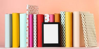 A row of colourful books with a tablet/kindle displayed at the front