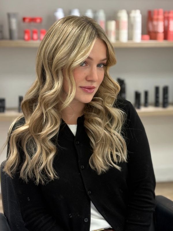 Blonde woman with wavy hair poses in a salon setting.
