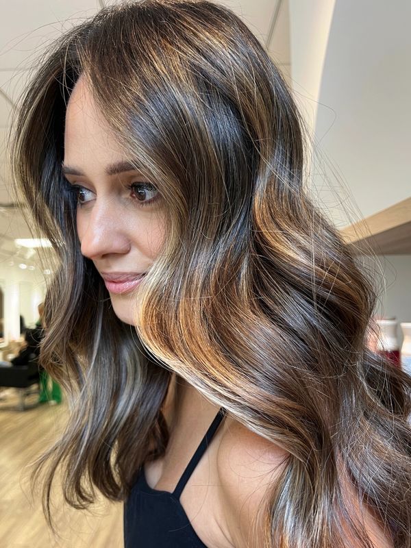 Woman with long, wavy hair featuring warm caramel highlights in a salon.
