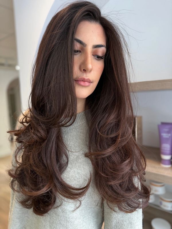 Woman with long, voluminous layered brown hair wearing a gray sweater.