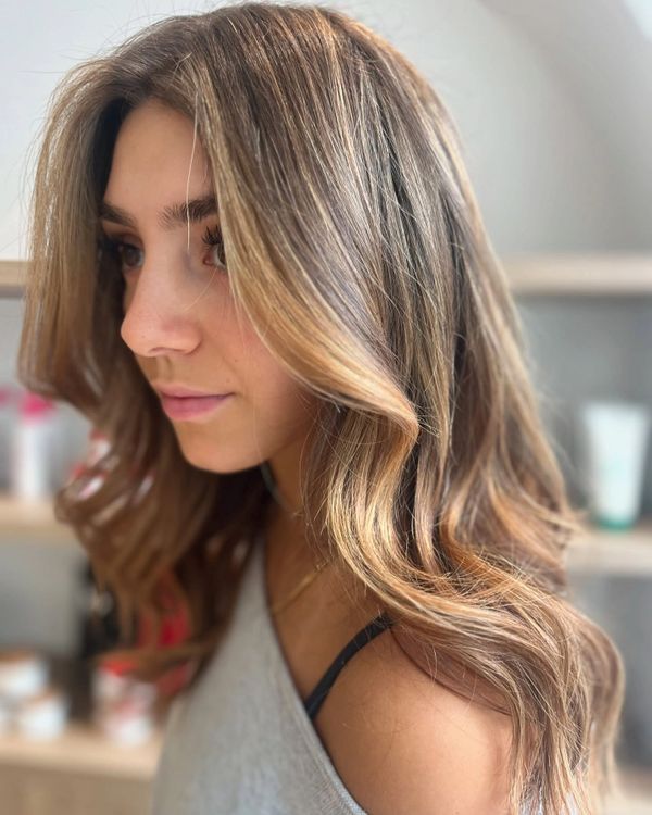 Young woman with long, wavy, highlighted hair looking to the side.