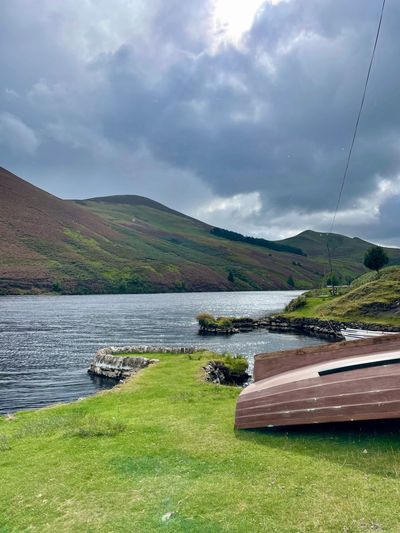 Lake with hills in background and rowing boats moored upside down on land at the shoreside.