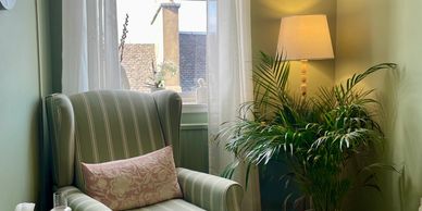 Comfy chair, green plant and floor lamp next to window creating a calm inviting space