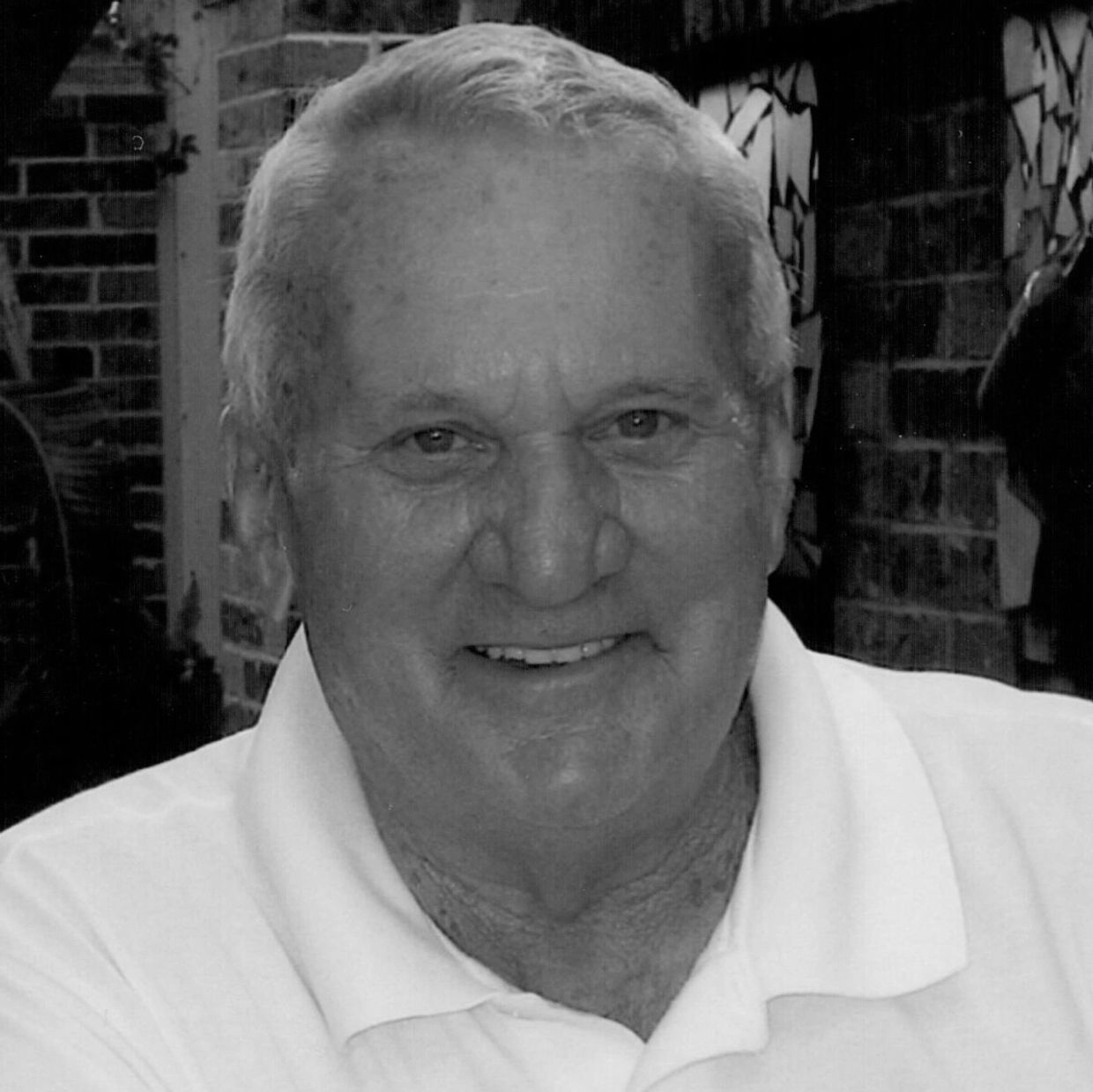 Smiling elderly man with blue eyes wearing a white polo shirt.