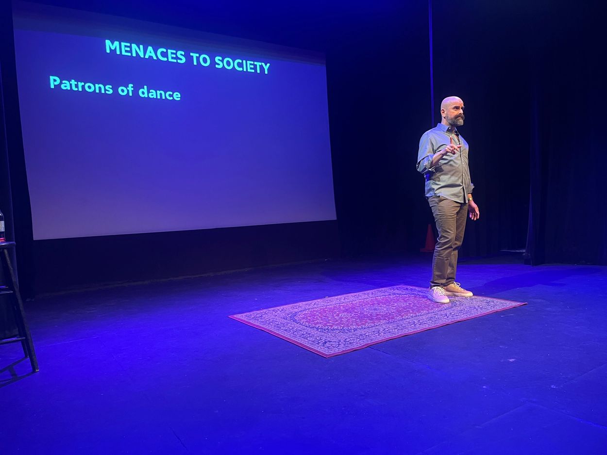 Haig "Hike" Chahinian stands before a screen that reads "Menaces to Society: Patrons of Dance"