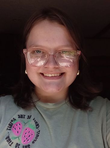 Smiling person wearing transparent glasses and a green t-shirt.