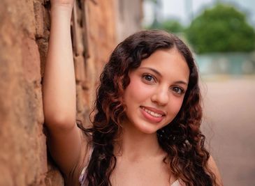 Smiling woman with curly hair leaning against a stone wall.