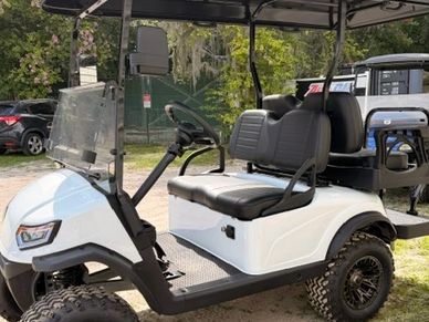 White golf cart parked outdoors with large tires and black seats.