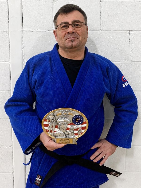 Man in blue judo gi holding a 2nd place trophy.