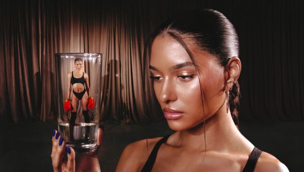 Woman holding glass with a miniature boxer inside.