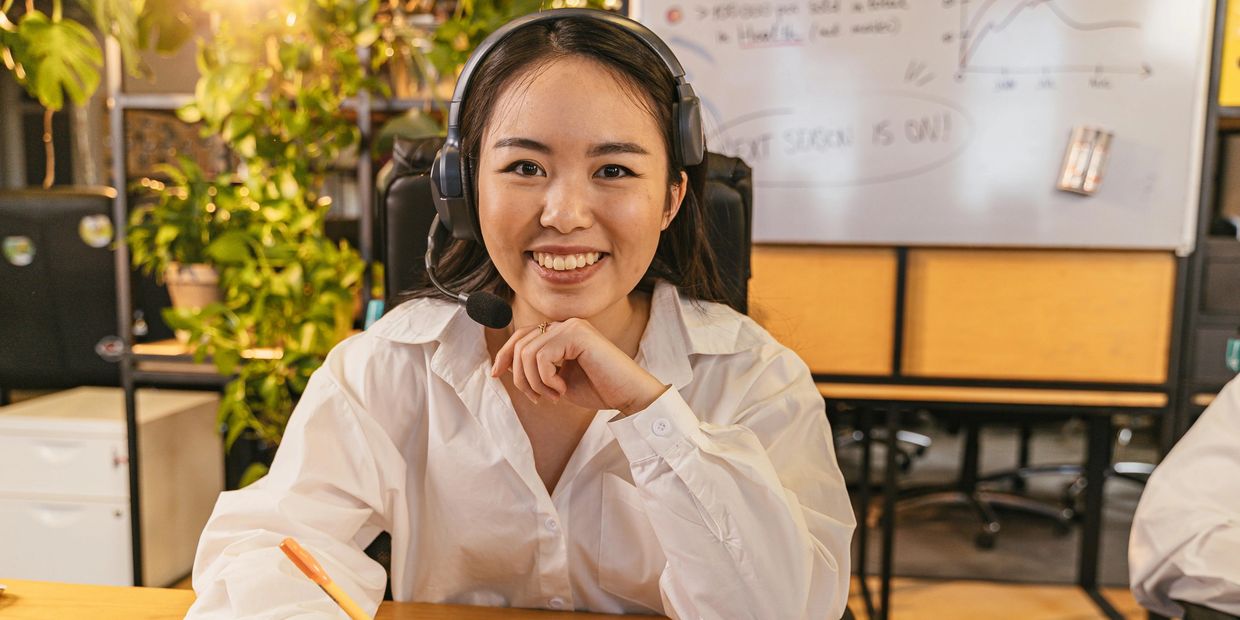 Smiling woman wearing headset and writing in notebook at a desk.