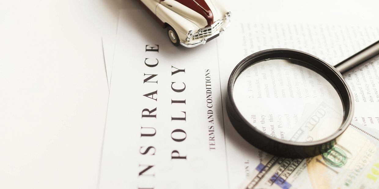 Magnifying glass on insurance policy with a toy car and money.