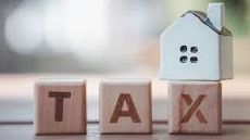 Real estate land tax concept image with wooden blocks spelling 'TAX' next to a small model house. To