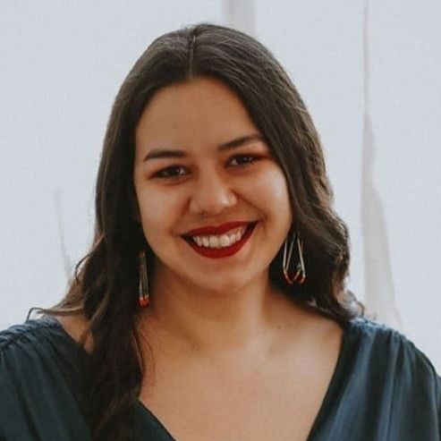A woman with dark hair smiling warmly in a dark top with dangling earrings.