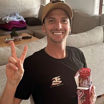 Smiling man making a peace sign and holding a boxed item.