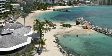 Tropical beach with clear water and resort buildings.